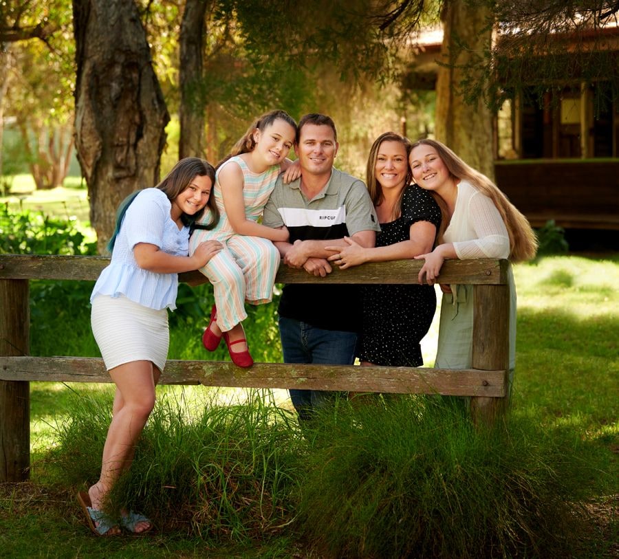 A family of six leaning on the fence rail in front of the cottage