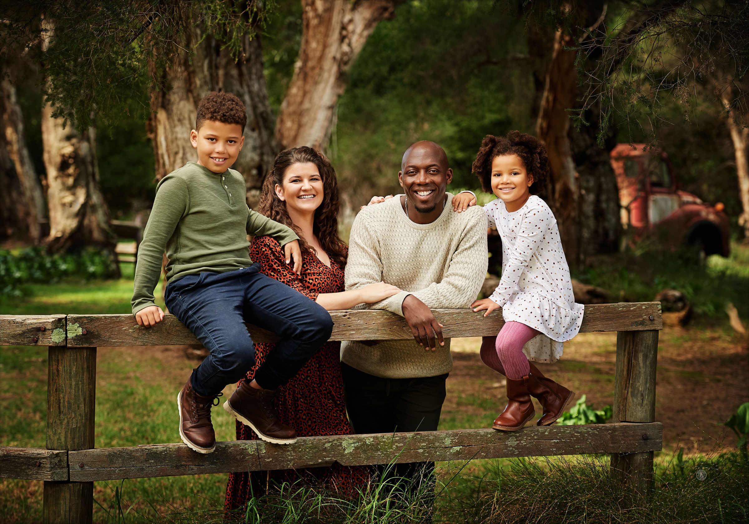 A family of four sitting on the farm fence under the paperbarks