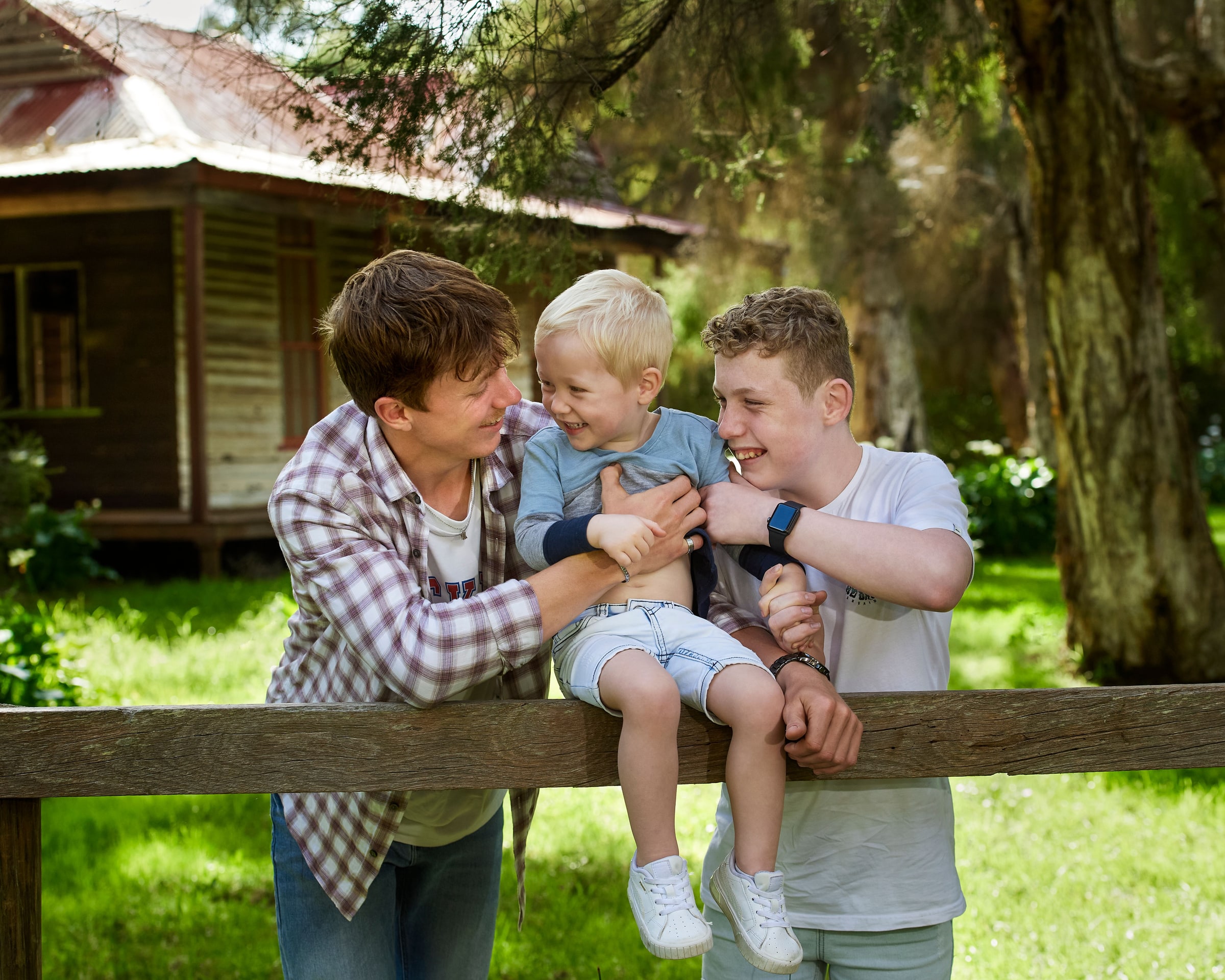 Two brothers laughing with their little brother on the fence