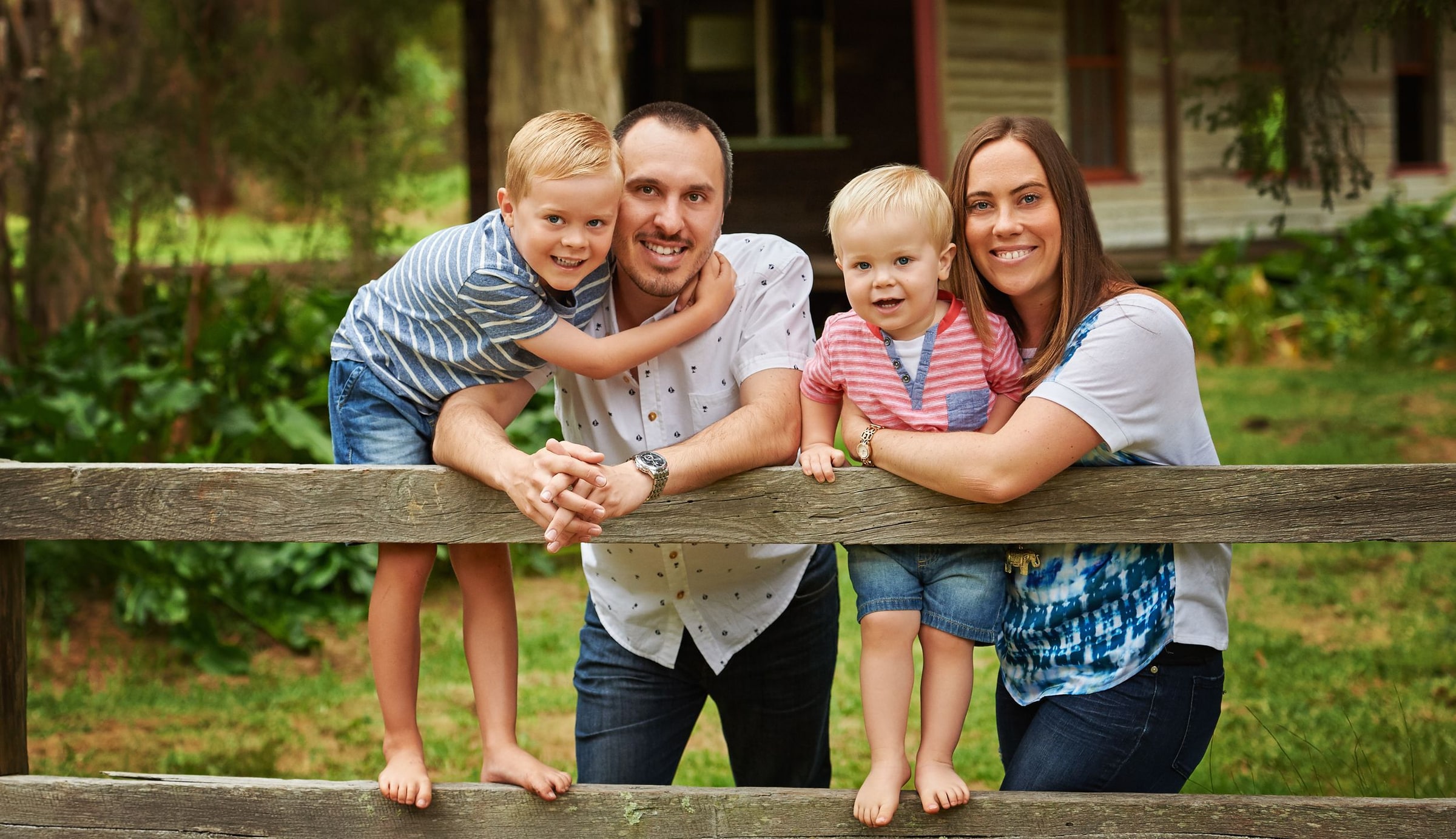 A family leaning over the timber fence rail in front of the cottage
