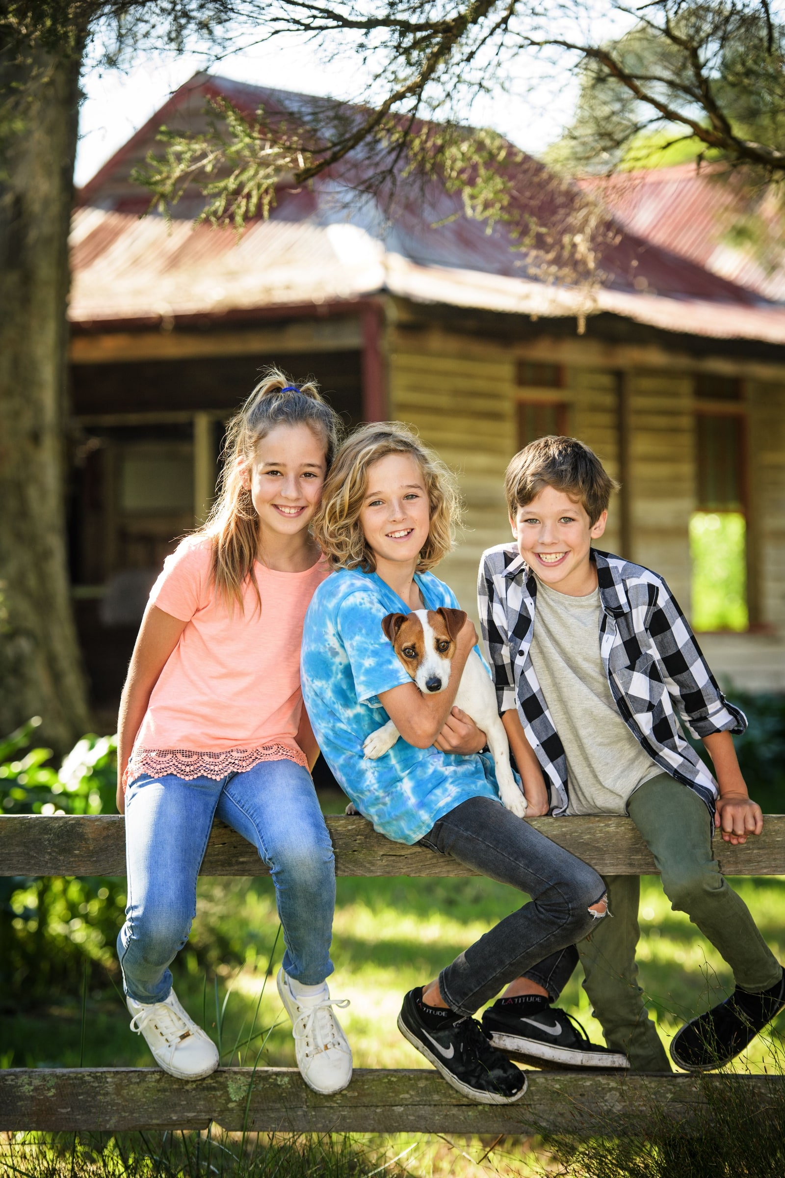 Three children and their dog sitting on the farm fence in front of the cottage