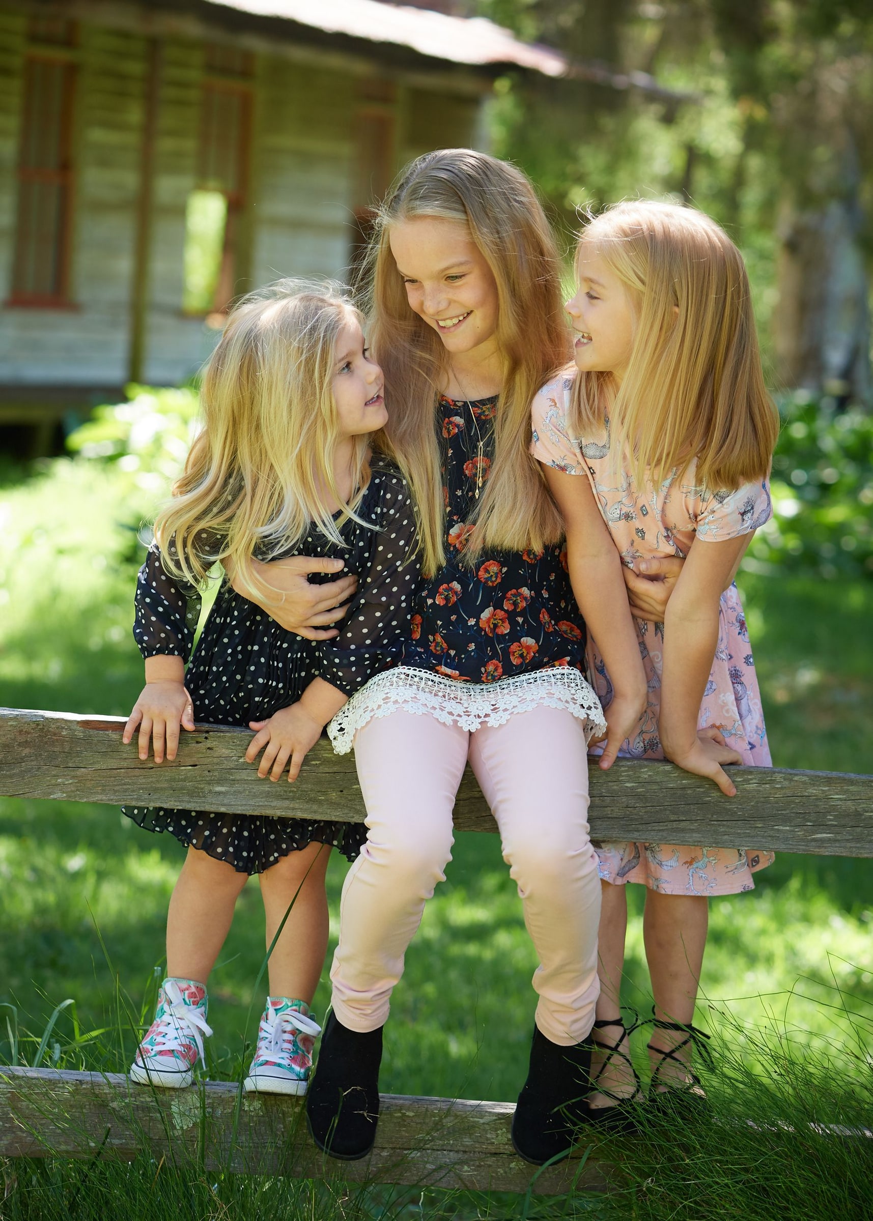Three young sisters sitting on the fence rail in front of the cottage