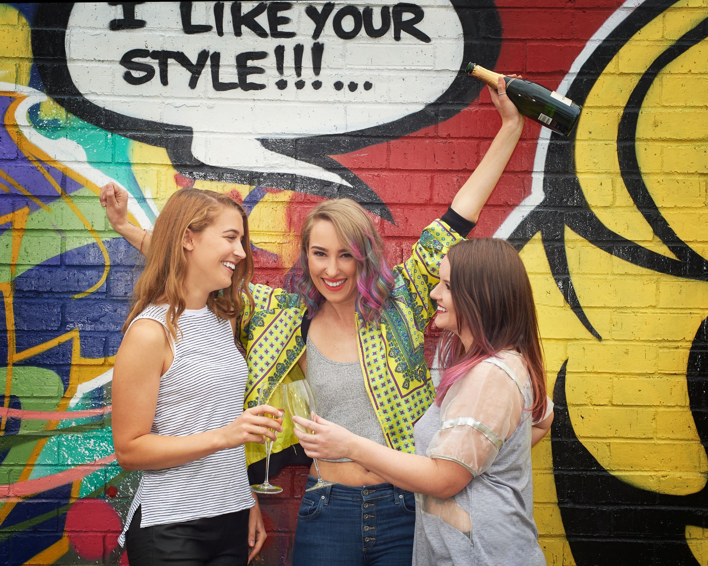 Three sisters laughing beside the pop art mural