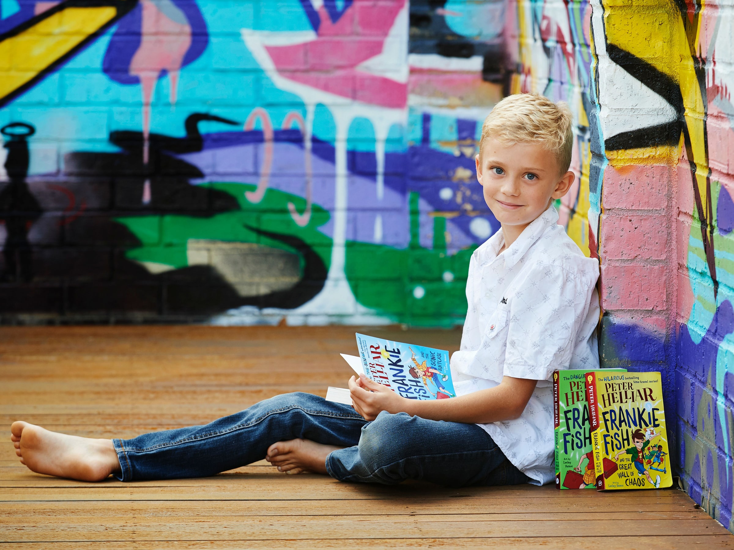 A boy reading on the floor beside the graffiti wall