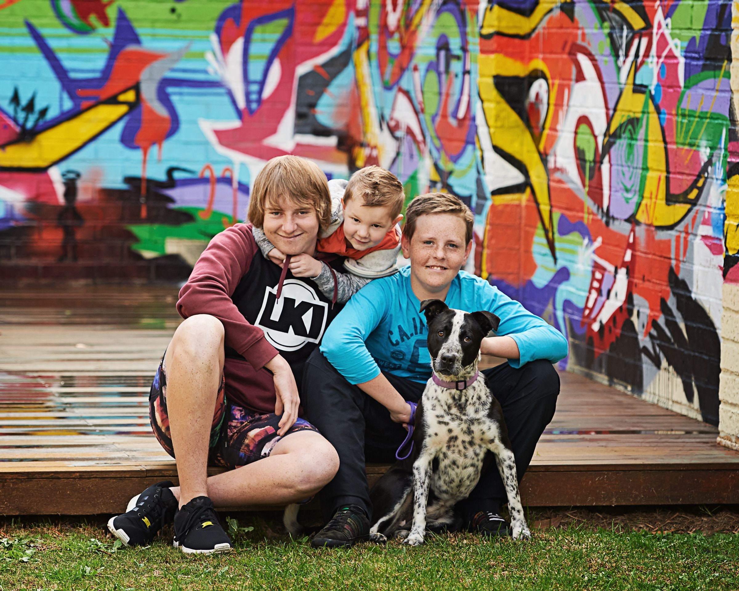 Three children and their spotted dog in front of the graffiti