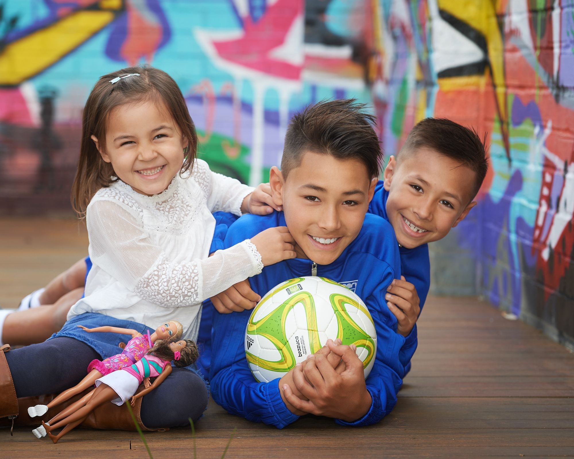 Three children with a soccer ball on the deck by the graffiti wall