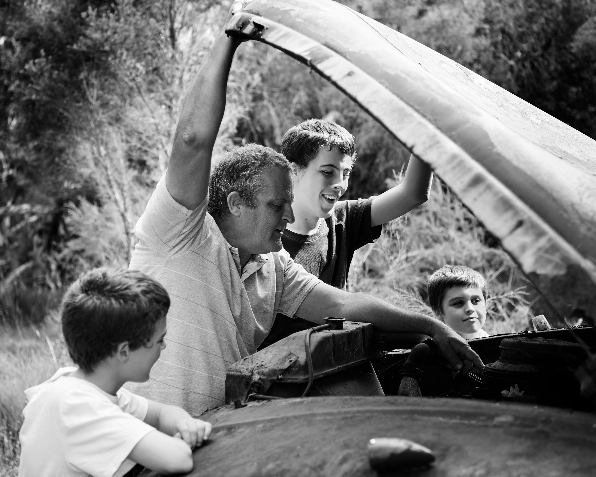 Black and white photo of a father and his sons under the truck's bonnet