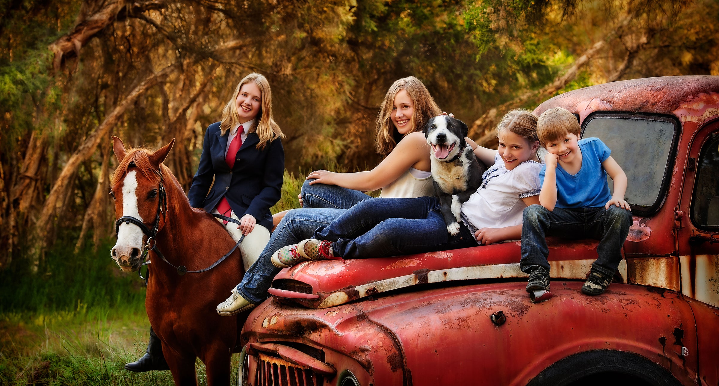 Teen with a chestnut horse beside three children and a dog on a rusty red truck
