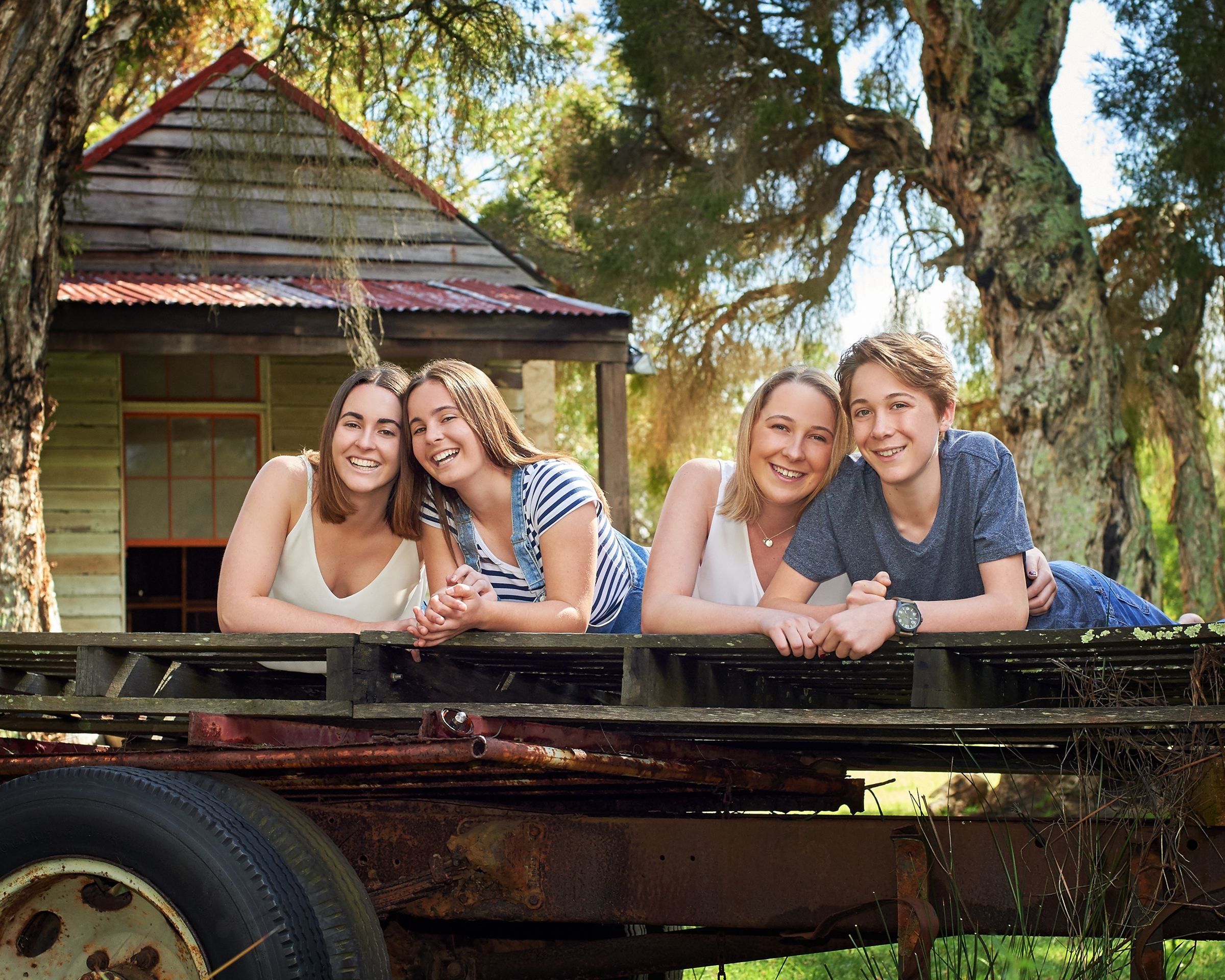 Four young people leaning on the tray of a vintage truck in front of a cottage