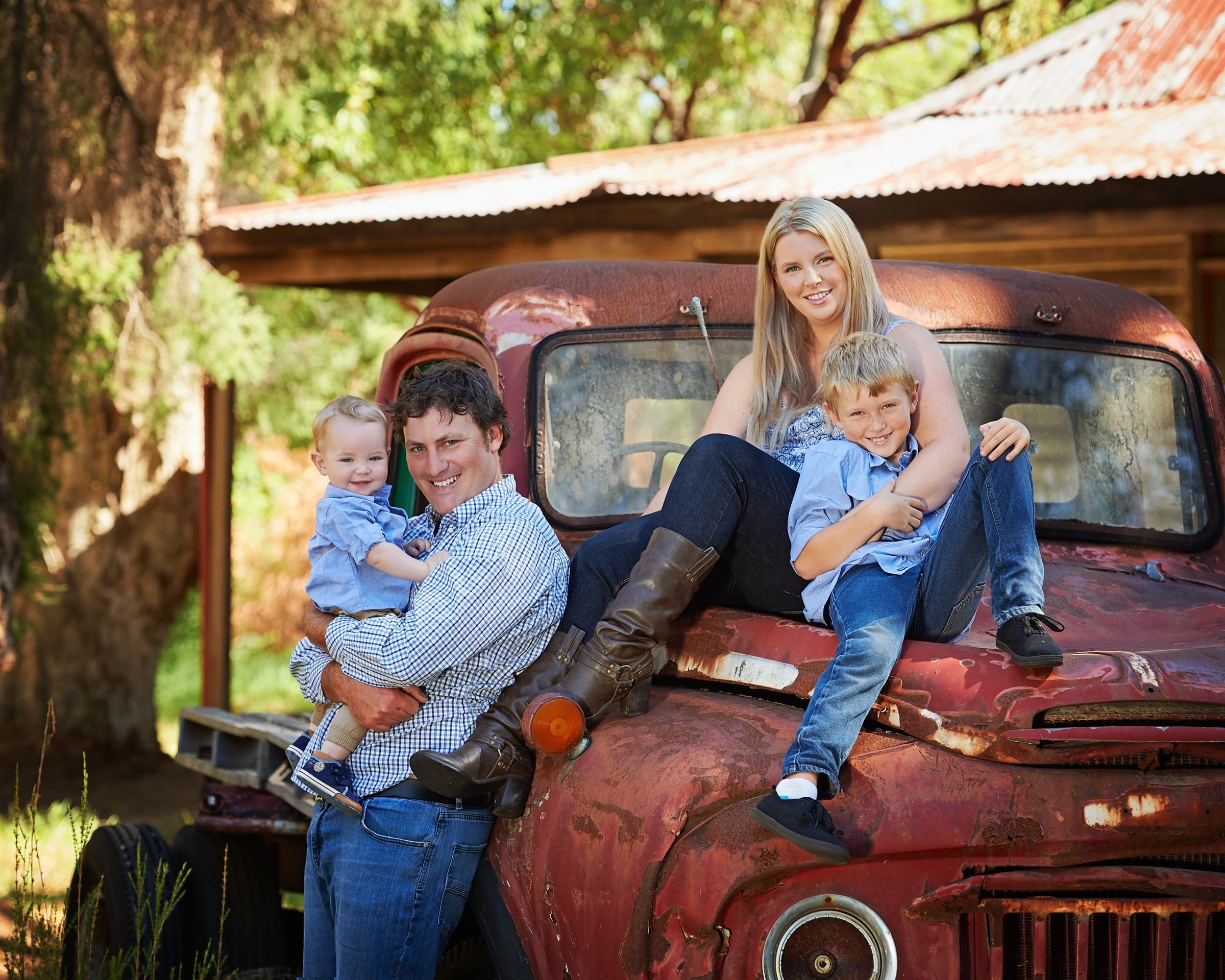 A family sitting on the bonnet of the truck in front of the cottage