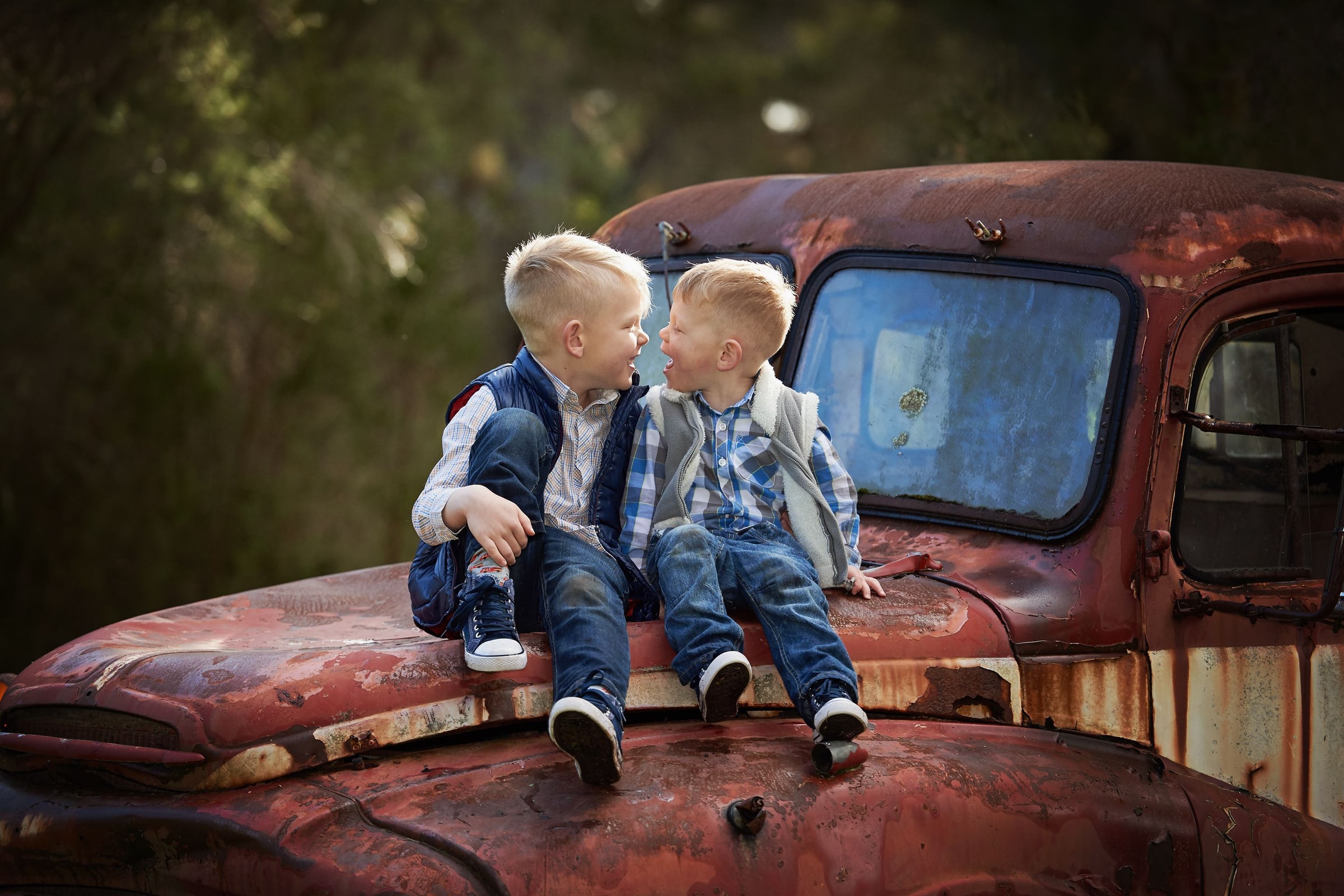 Two young brothers sitting on the truck's rusted bonnet