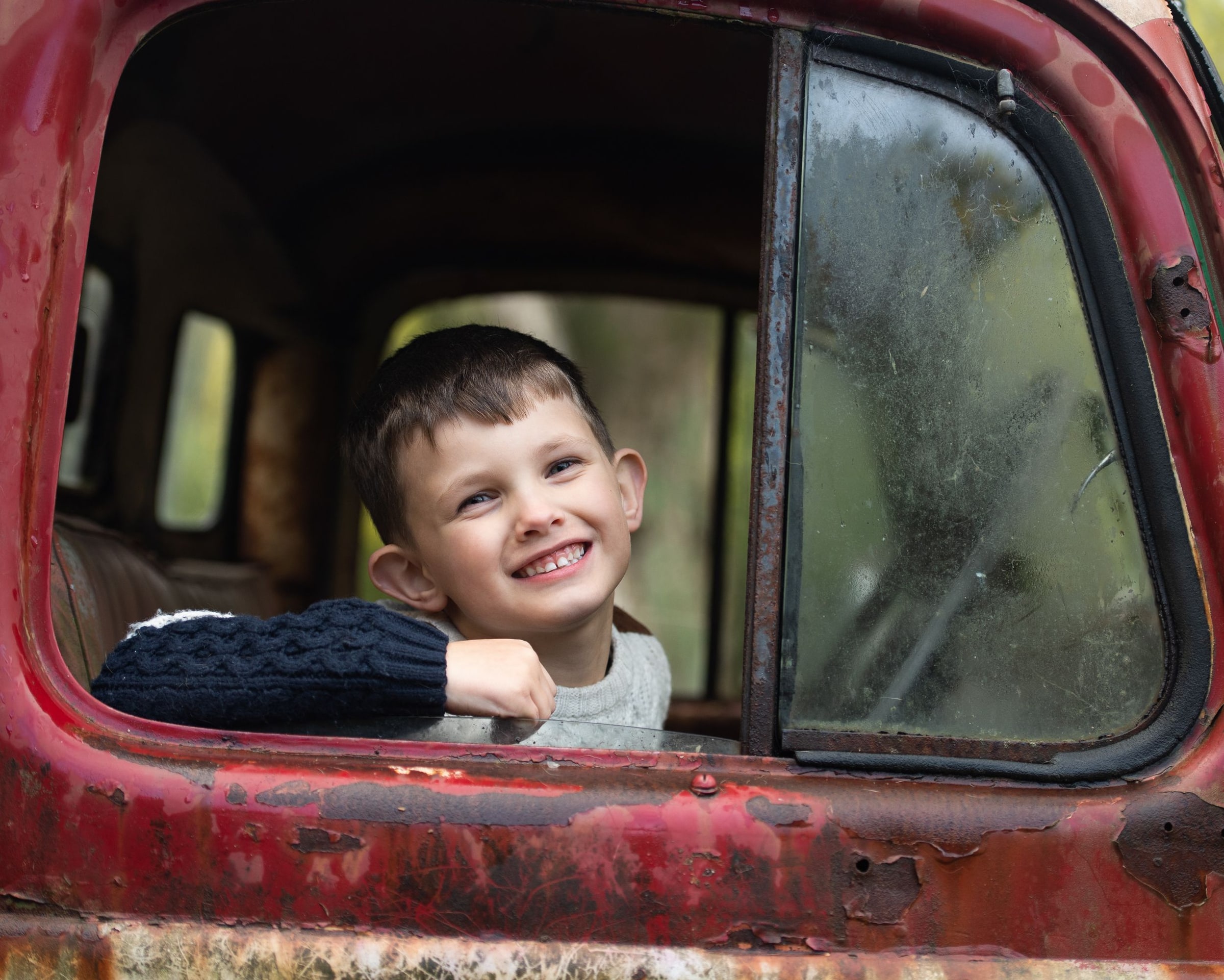 A smiling boy looking out the window of the red truck