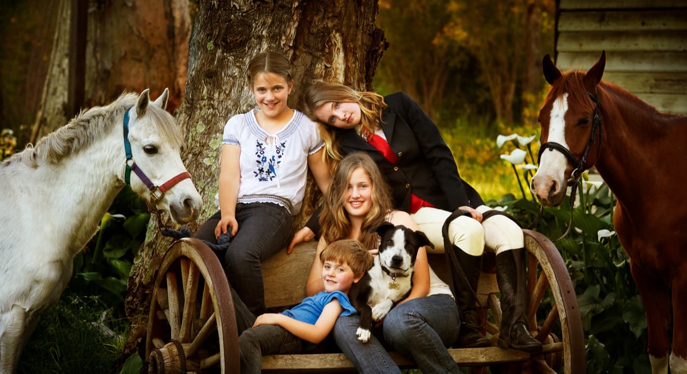 A family with their two horses and dog around an old wooden cart