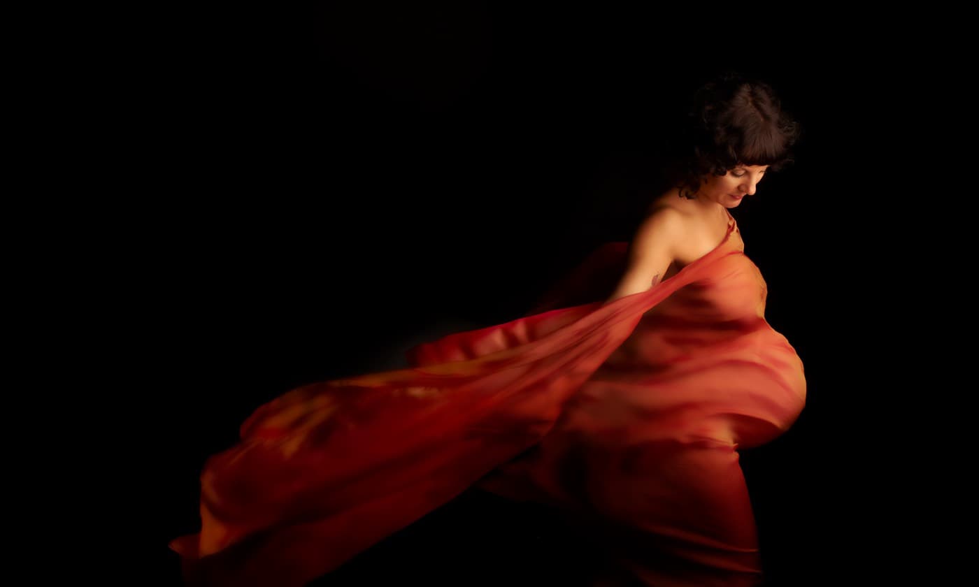 A woman draped in red fabric against a black background