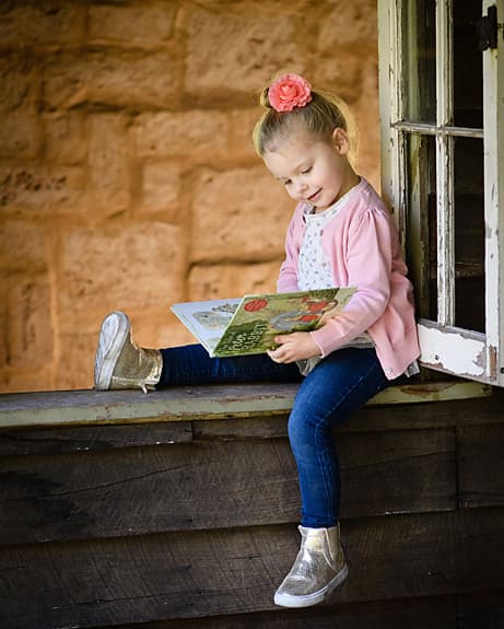 A little girl reading a picture book on a sandstone windowsill