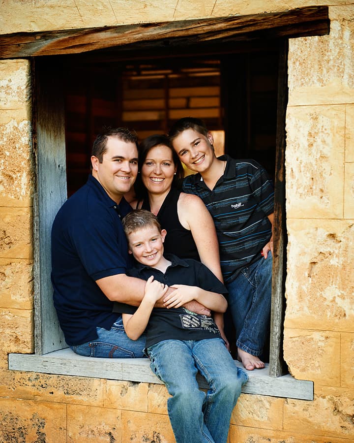 A family of four together in the window of a sandstone cottage