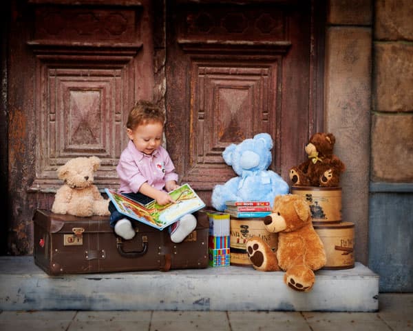 A toddler reading among teddy bears and old suitcases at the Egyptian Doors