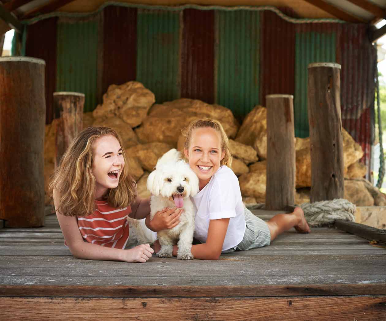 Two girls laughing with their fluffy white dog in the shed