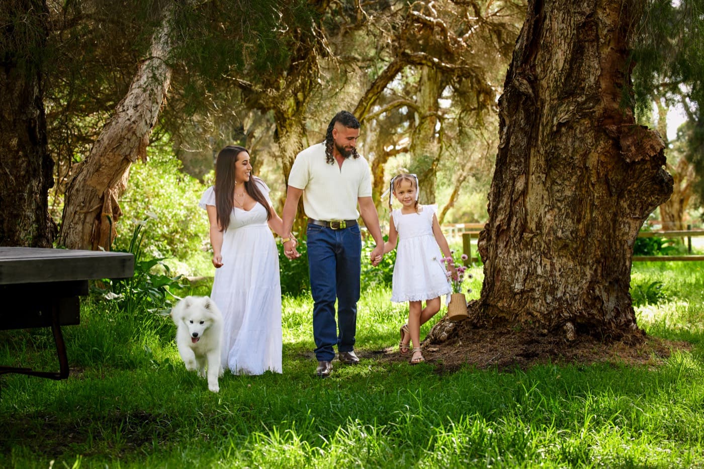 A family walking with their white dog under the trees