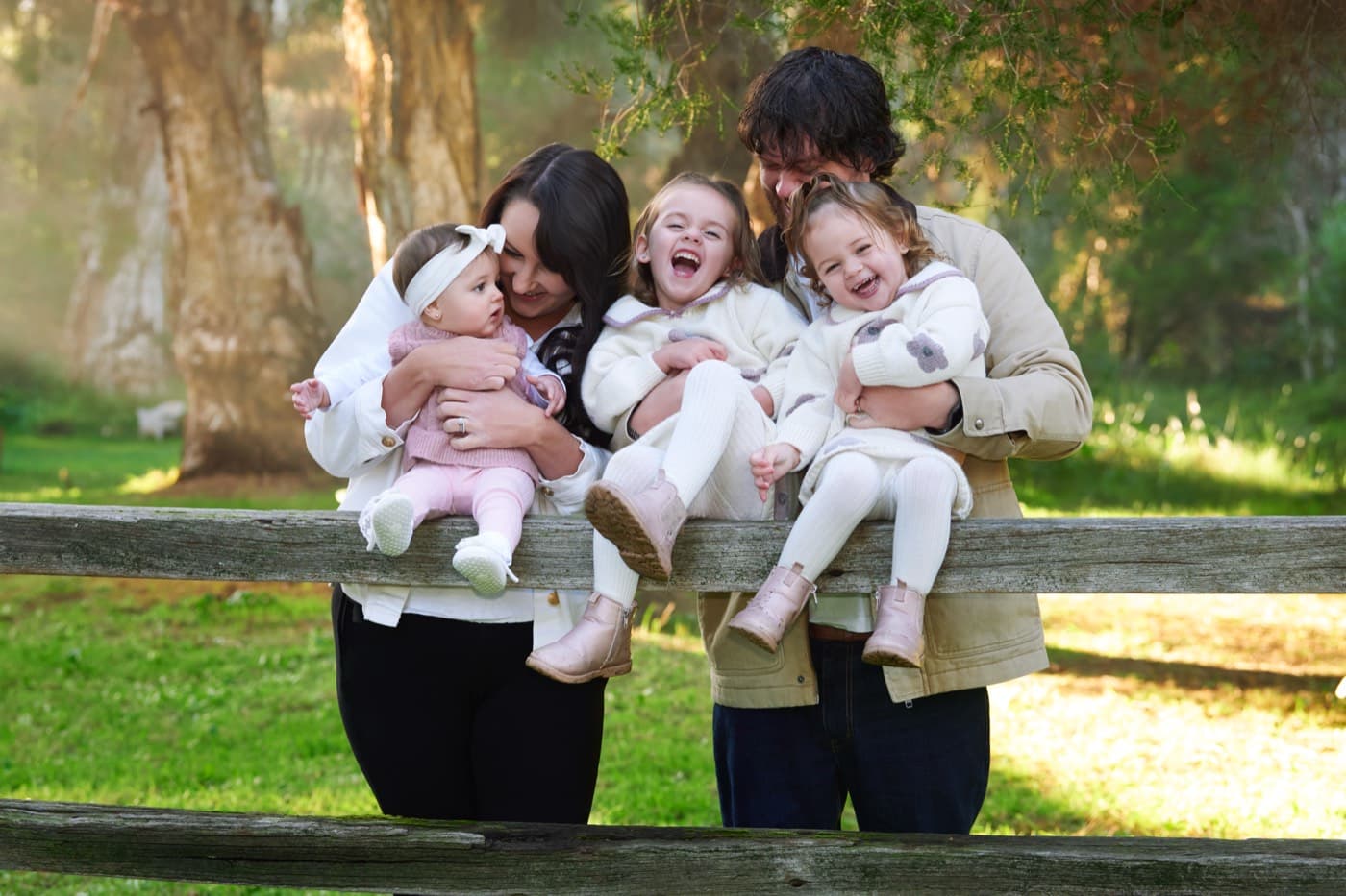 A family holding three little ones along a timber fence