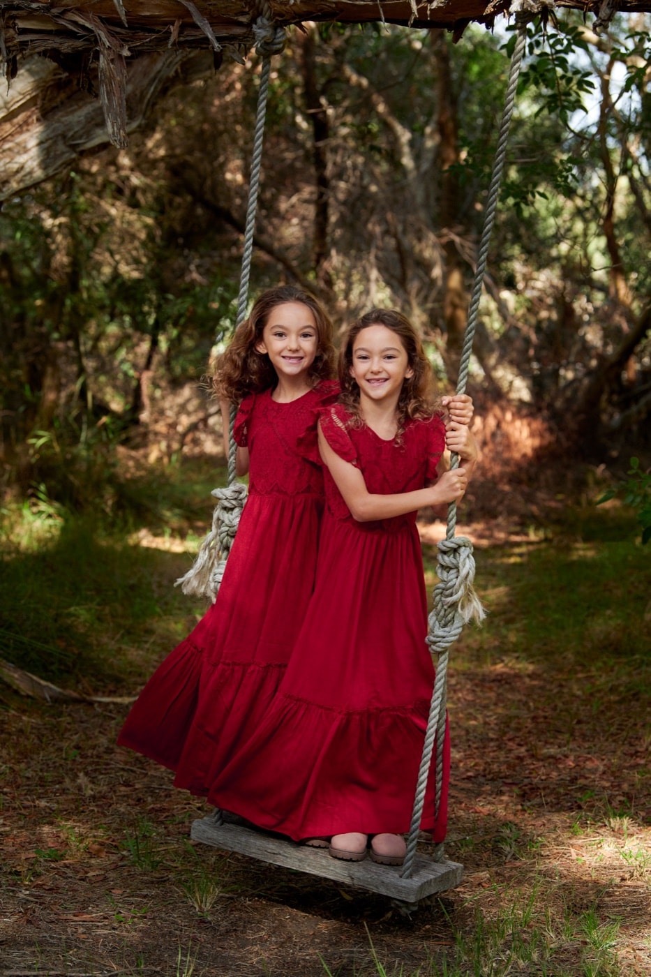 Two sisters in matching red dresses on the tree swing