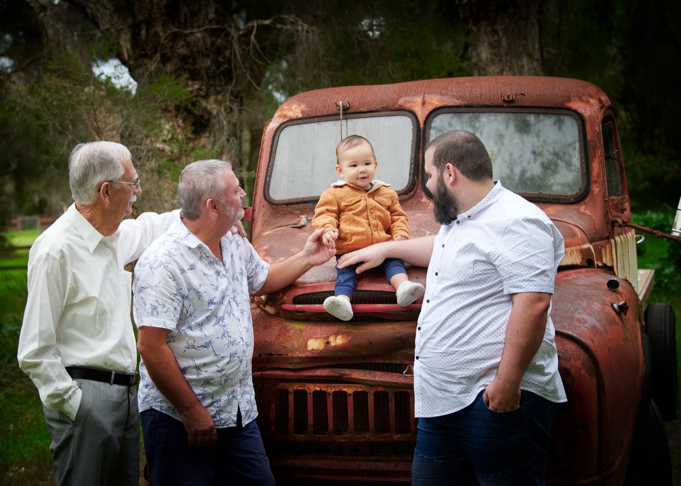 Three generations of men with a toddler on the vintage red truck