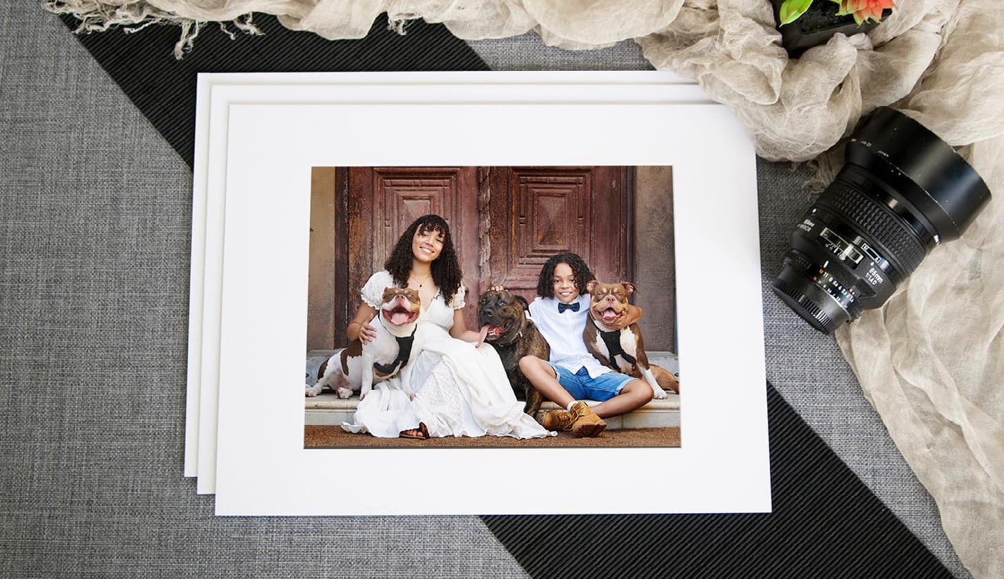 A matted art print of a family, resting on a woven mat beside a camera lens
