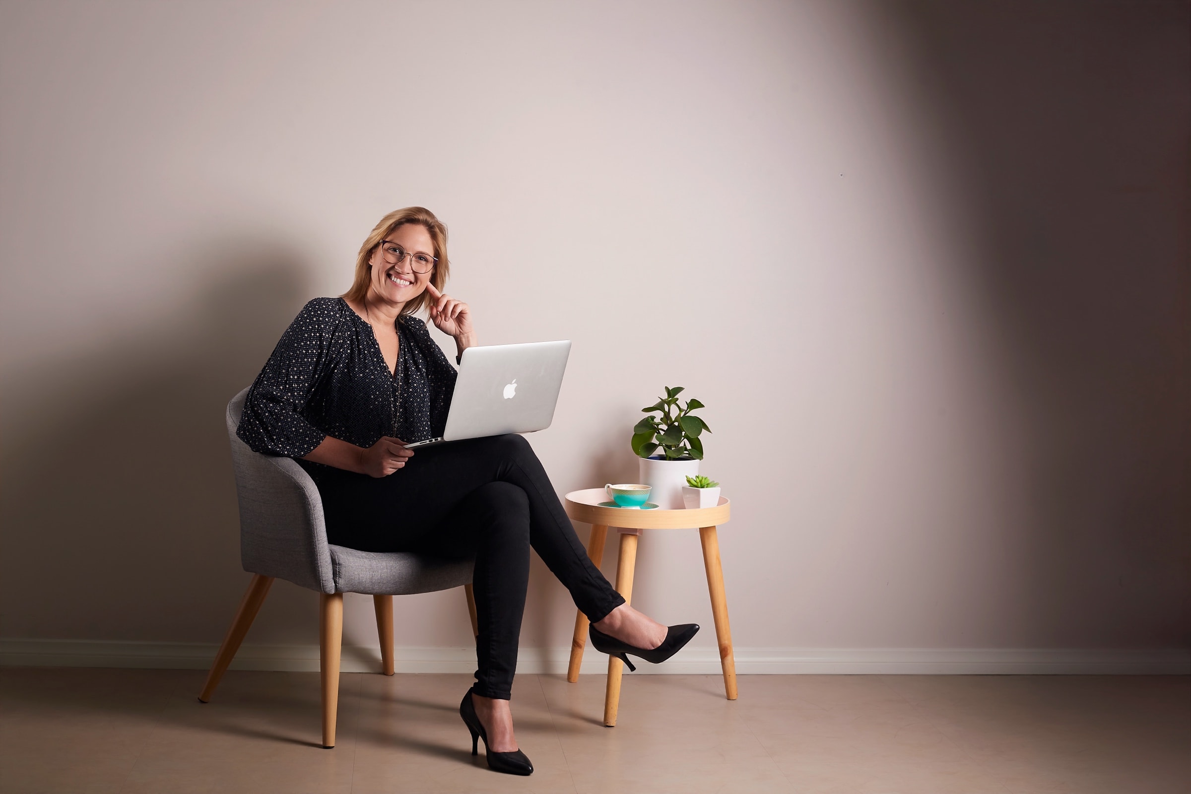 A businesswoman with her laptop, seated in a grey armchair in the studio