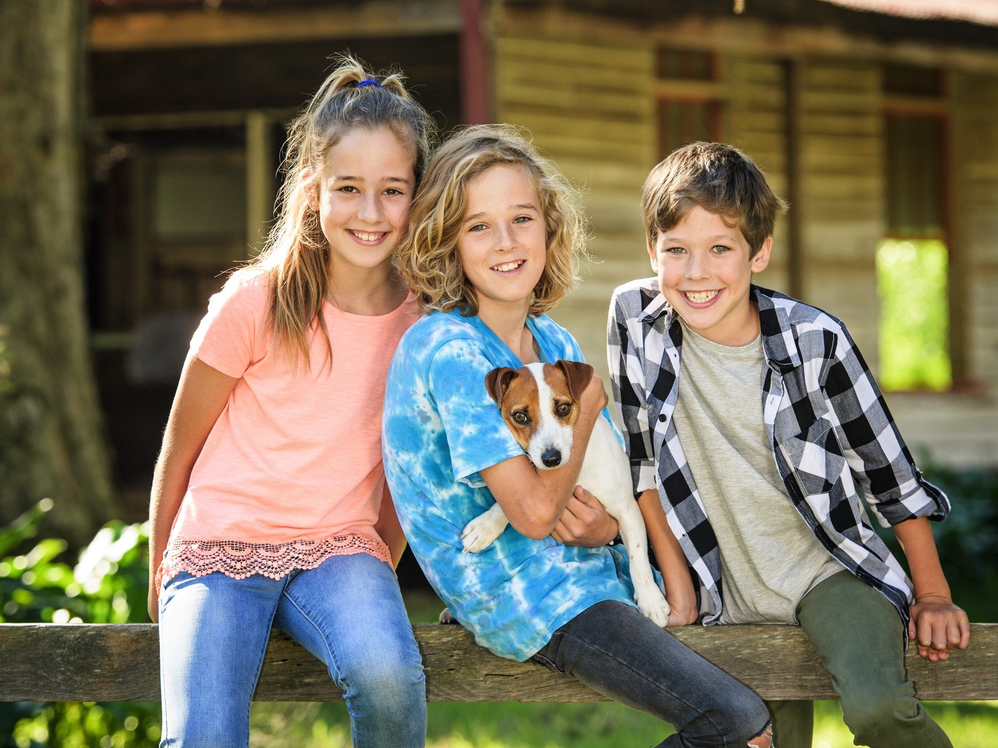 Three children and their dog sitting on the farm fence in front of the cottage