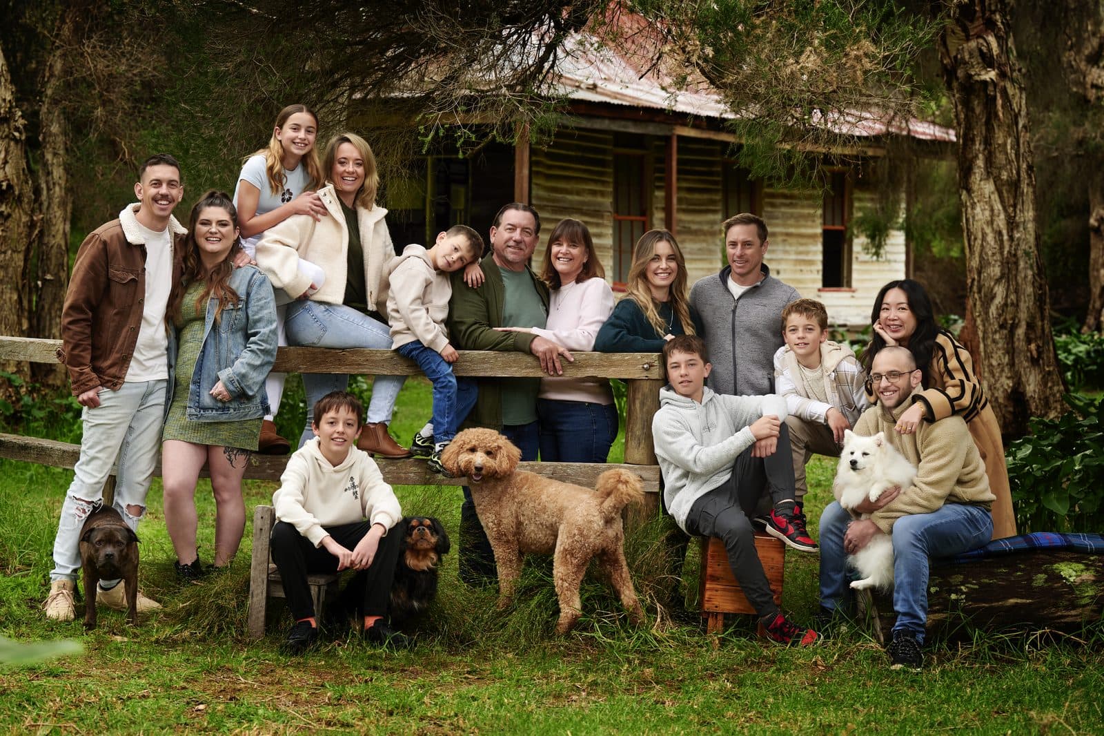 An extended family of fourteen and their four dogs at the farm fence in front of the cottage