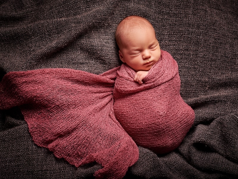 A sleeping newborn swaddled in a soft pink wrap