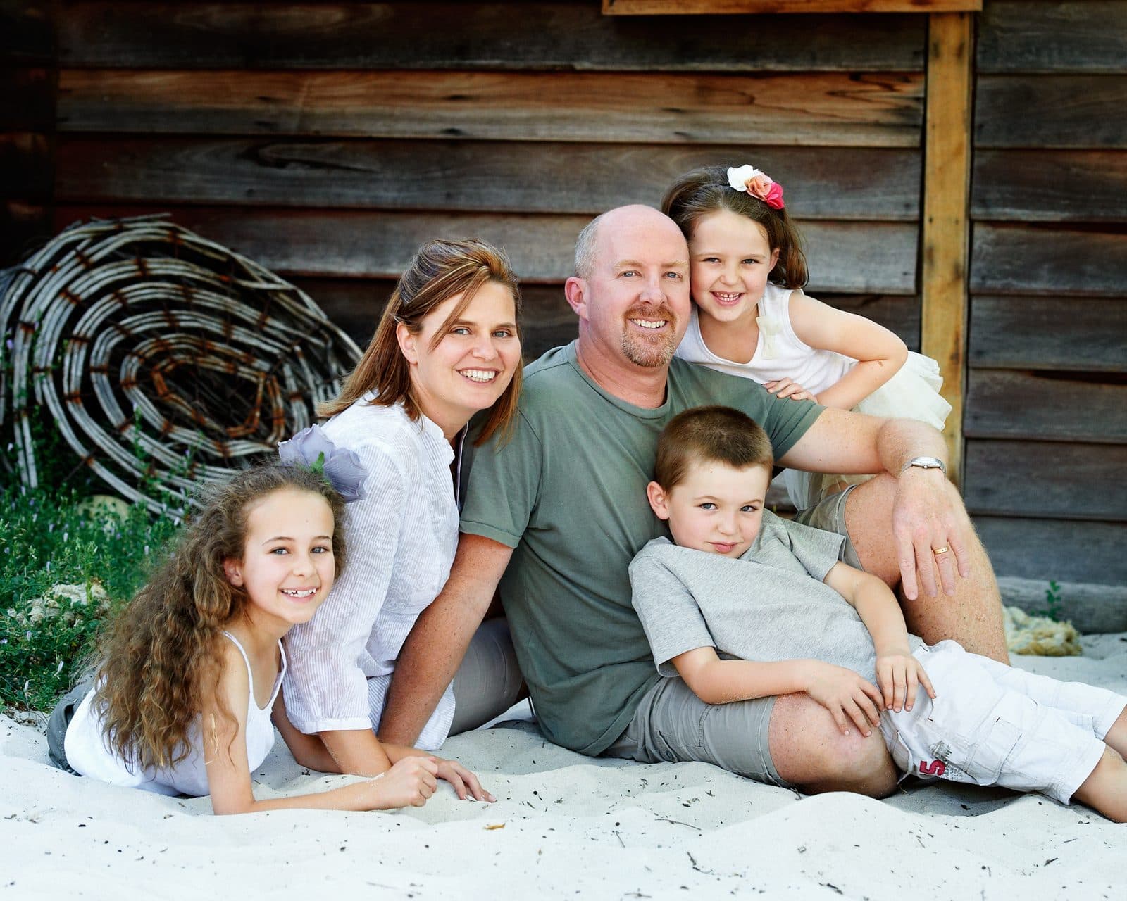 A family of five on the sand in front of the boat shed