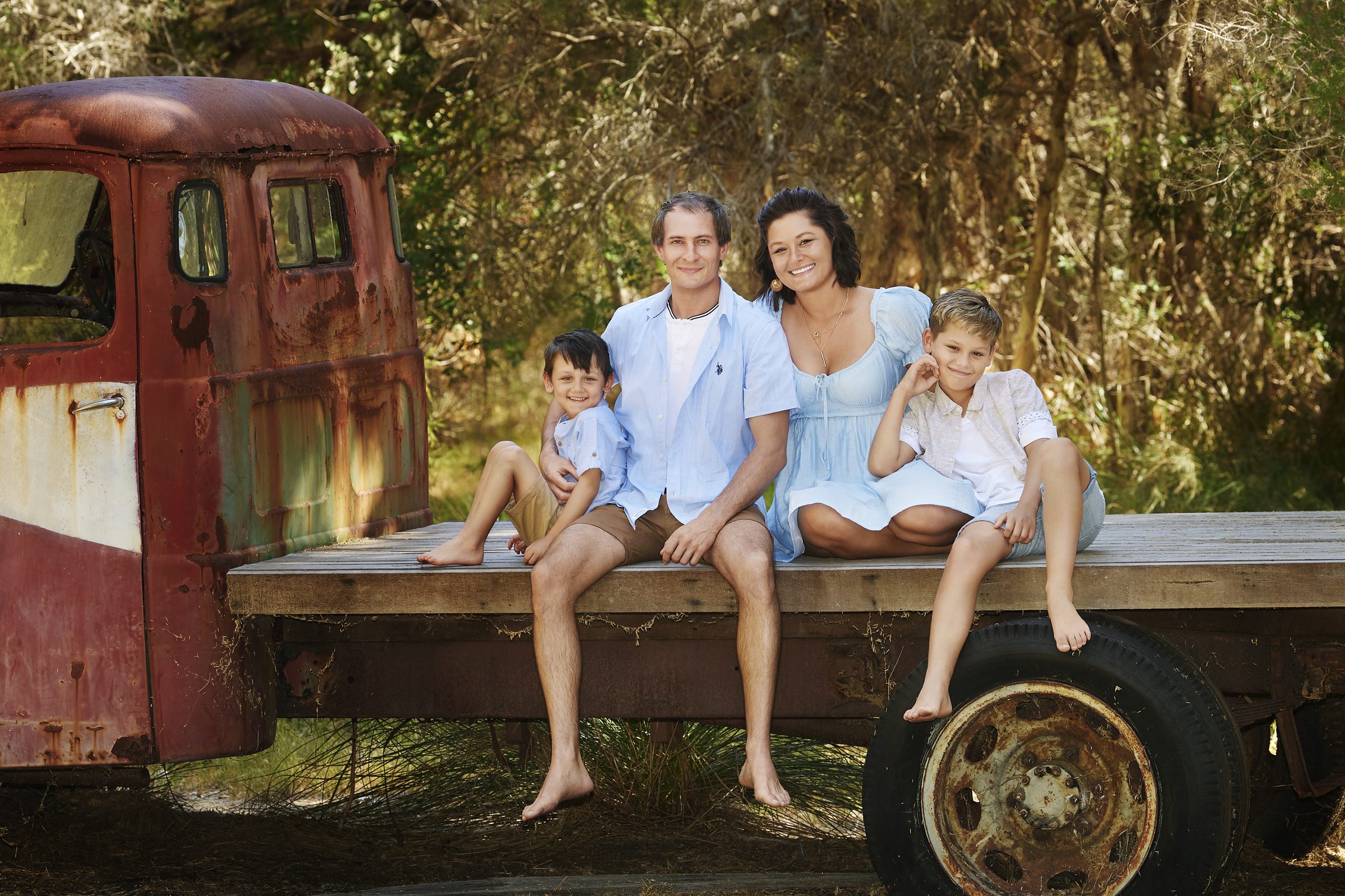 A family of four sitting barefoot on the back of the old red truck