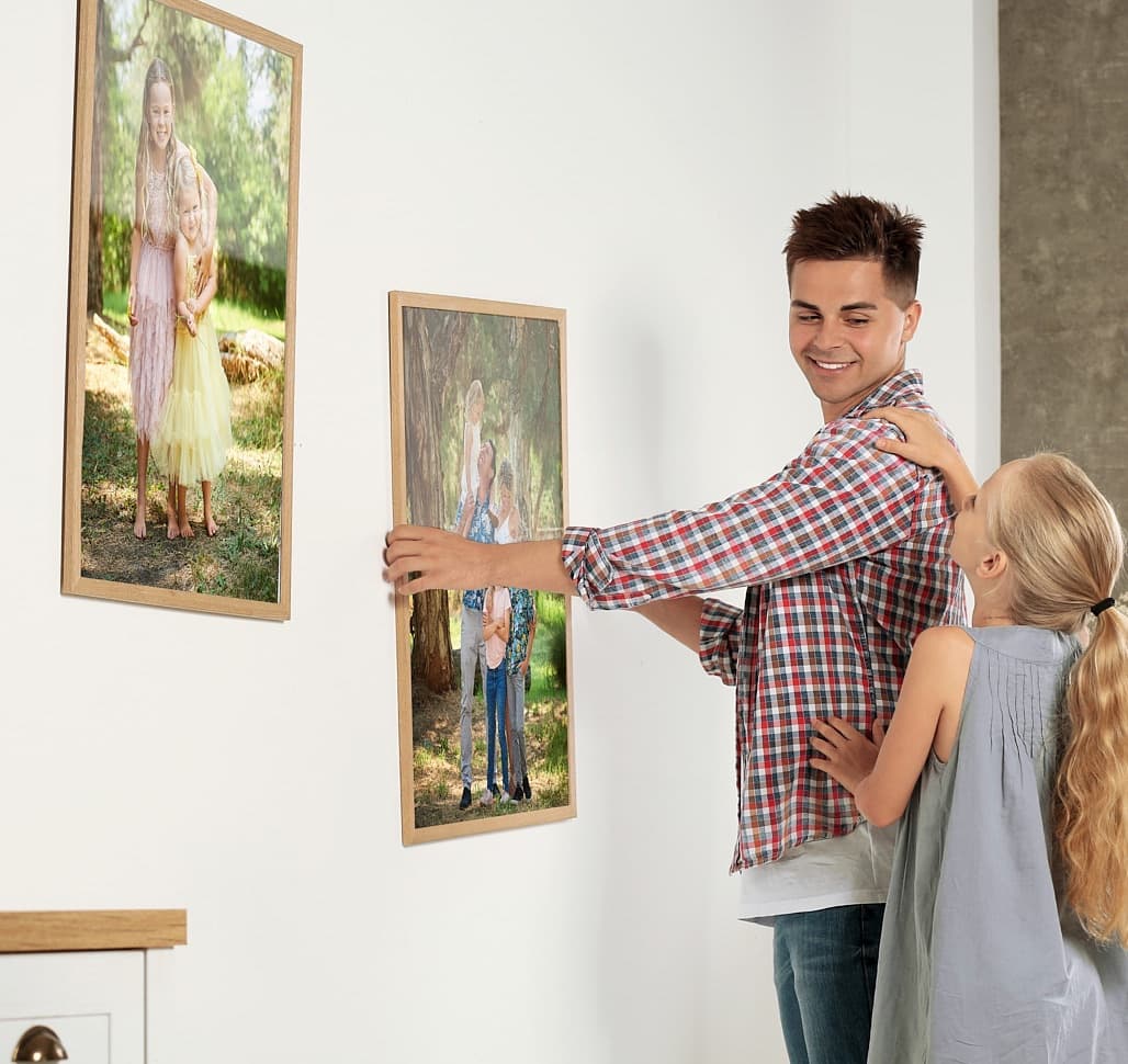 A father and his daughter hanging framed family portraits on a white wall