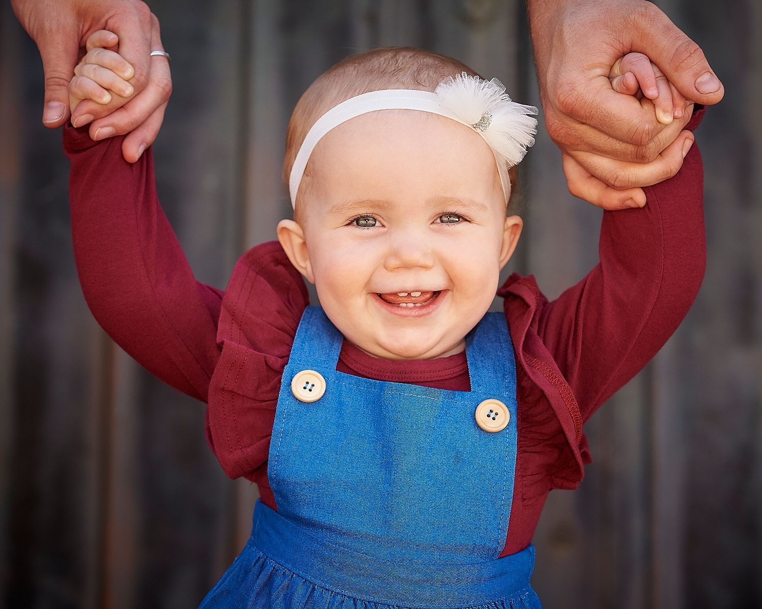 A laughing baby girl holding her parents' hands