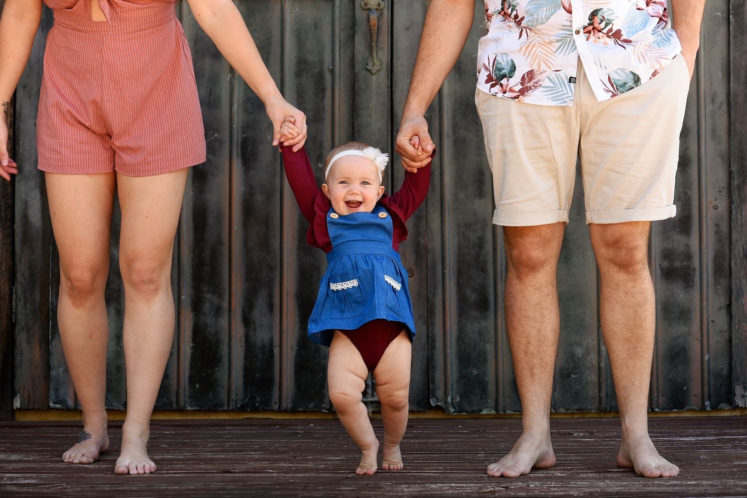 A toddler walking between his parents, holding their hands