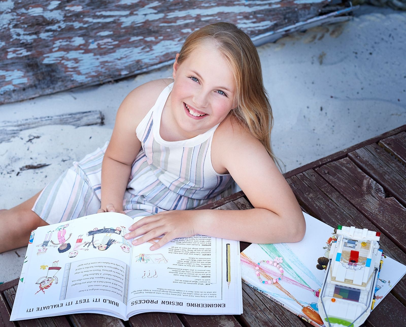 A smiling girl lying on the boards with an open book