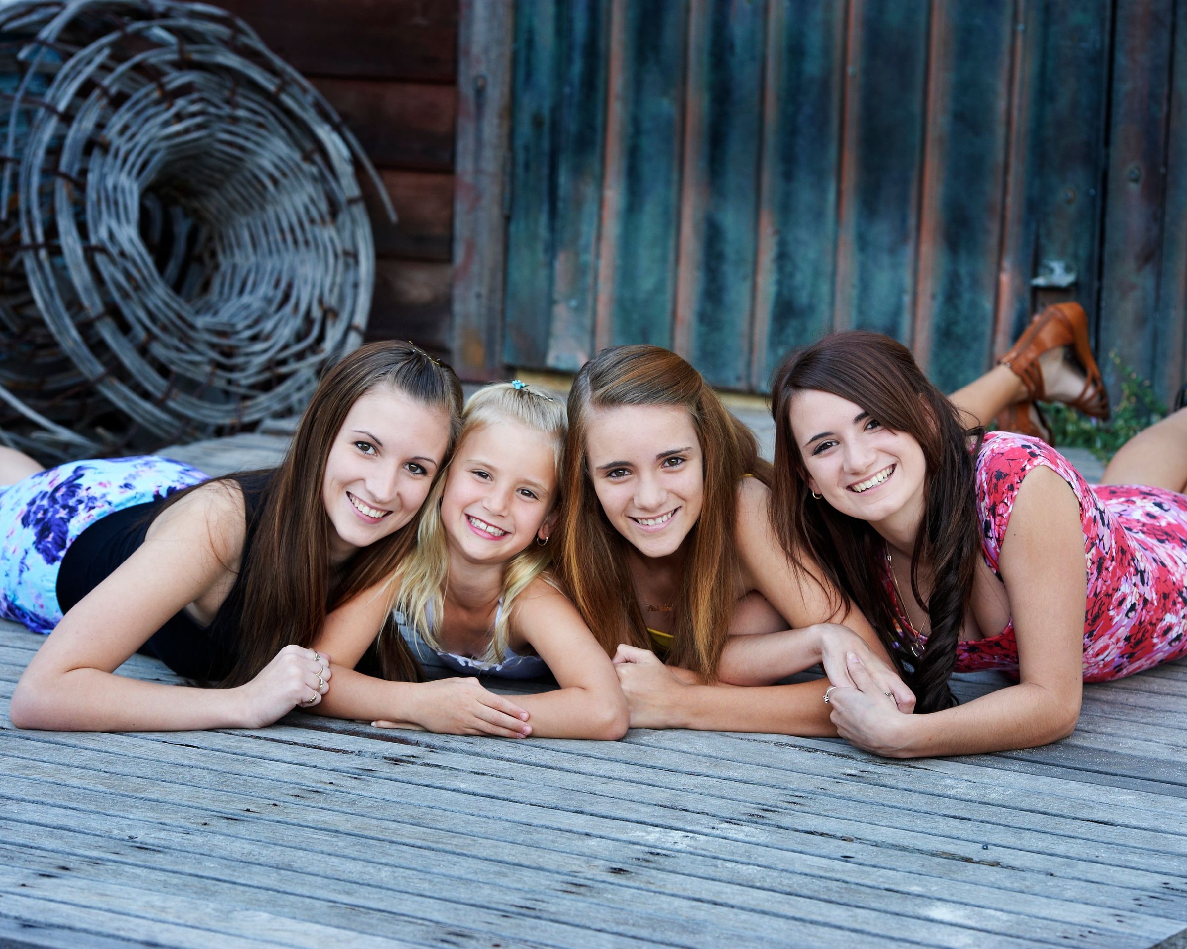 Four sisters lying on the timber boards in front of the boat shed doors
