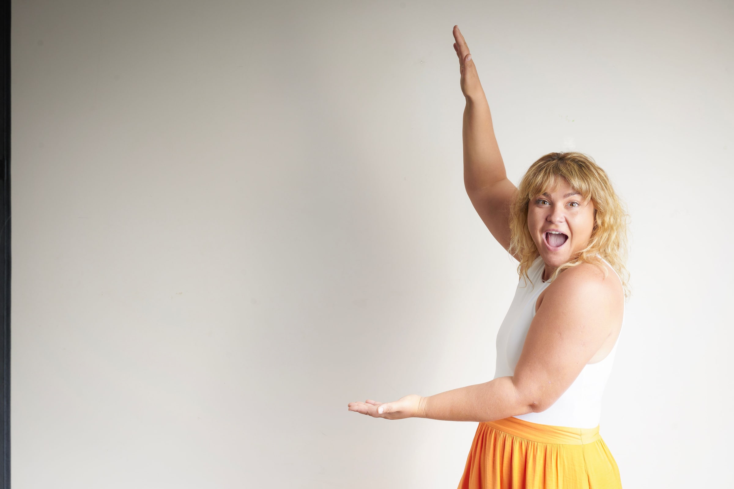Woman in a white top, mouth wide open, stretches one arm up and one out