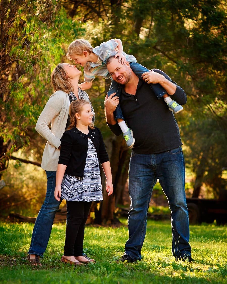 Father carrying a young boy on his shoulders beside mother and daughter in sunlit bushland