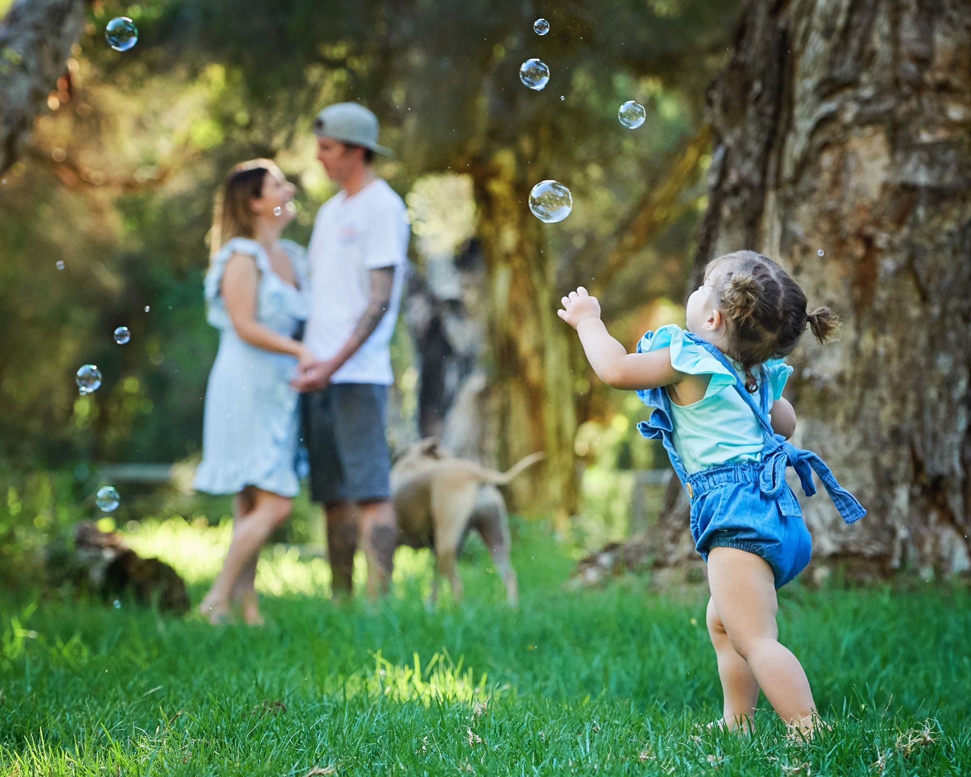 A toddler chasing bubbles while her parents watch