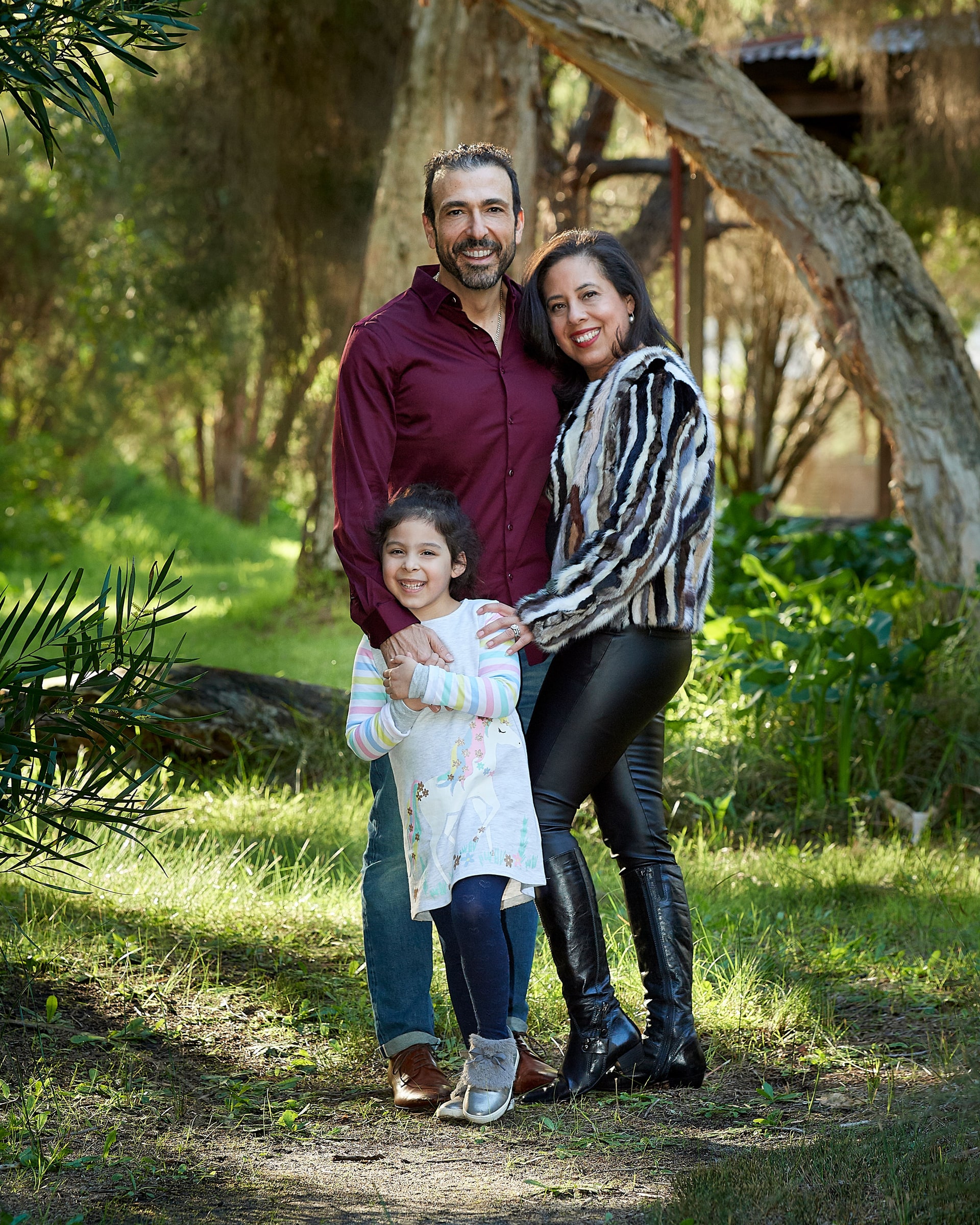 Mother, father and young daughter standing close together on a sunlit bushland path
