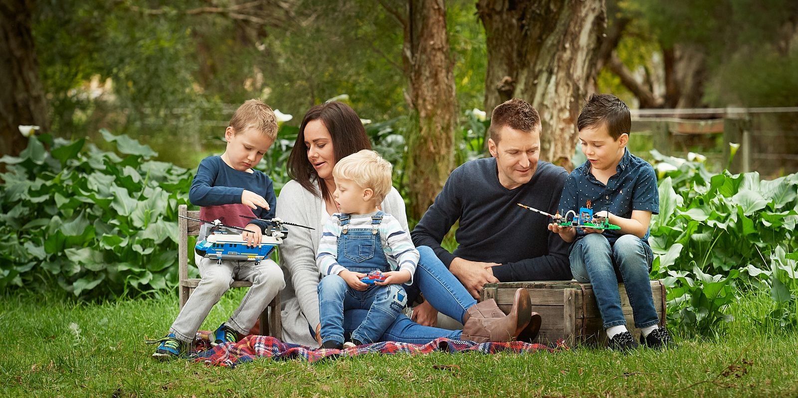 Parents and three young boys playing with toys on a tartan picnic rug in bushland