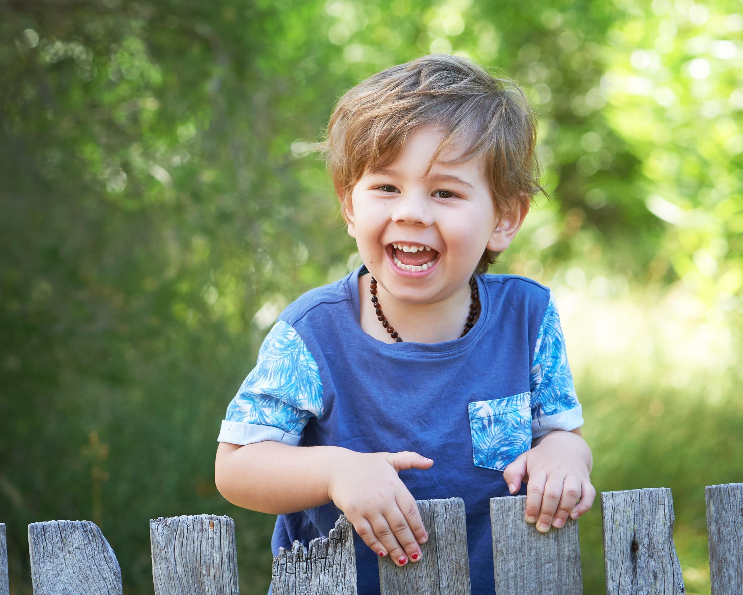 Young boy laughing as he leans over a weathered wooden fence in the bushland