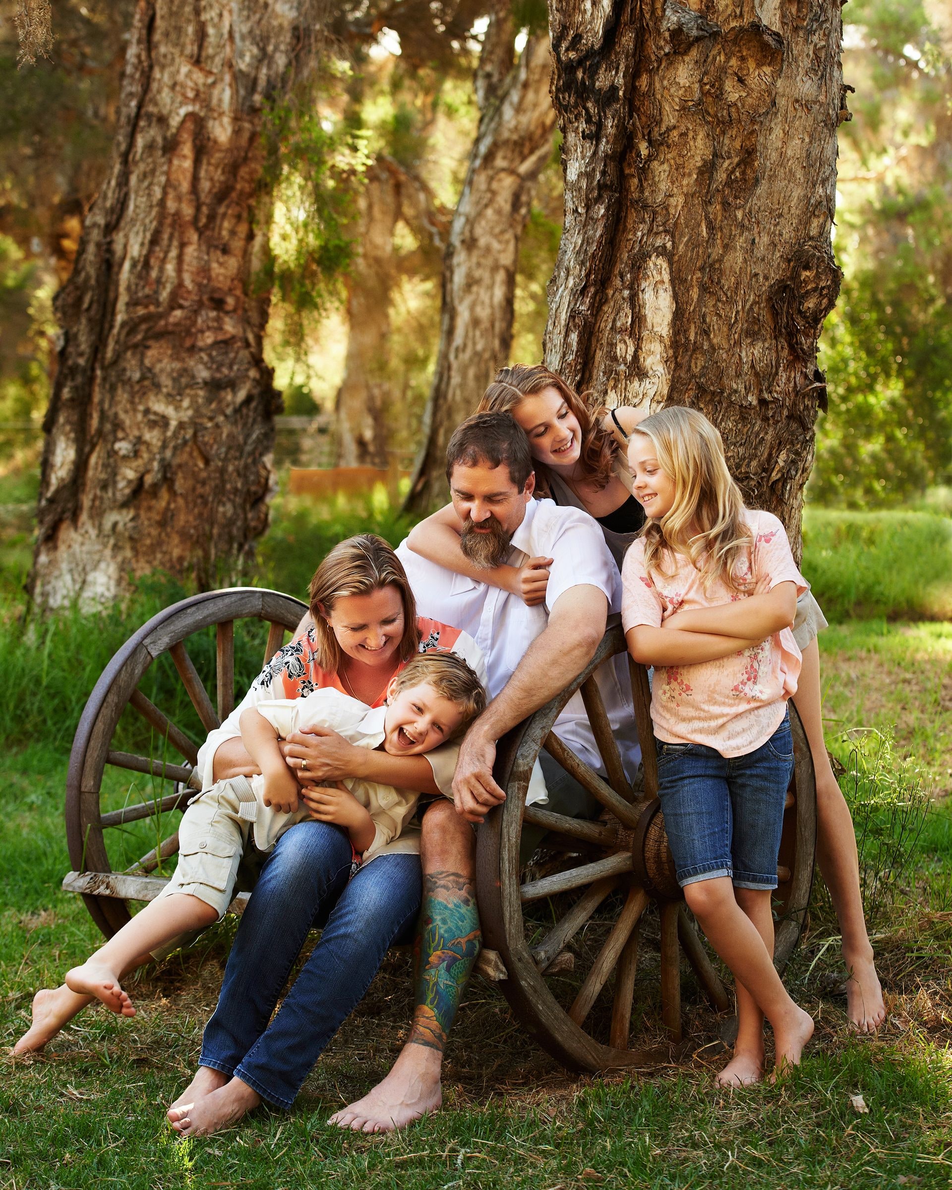 A family of five relaxing around an old wagon wheel under the paperbarks