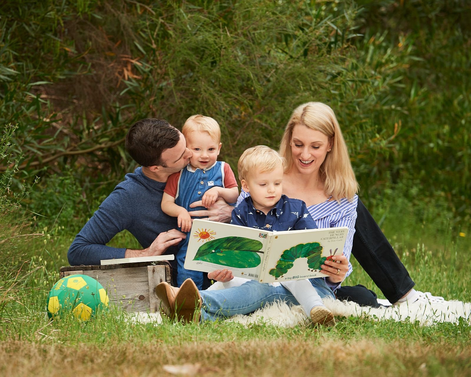 Parents reading a picture book with their two young boys on the grass