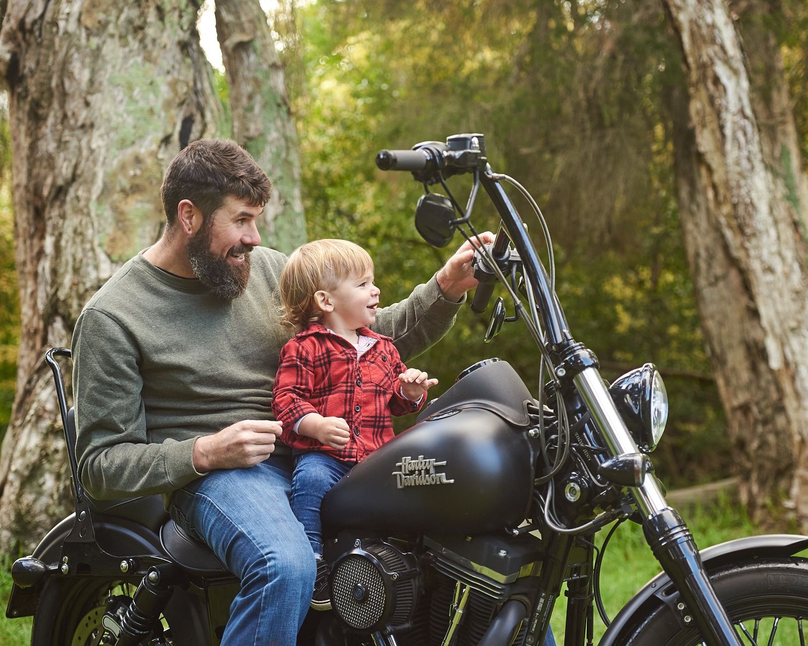 A father and son sitting on a motorbike among the paperbark trees