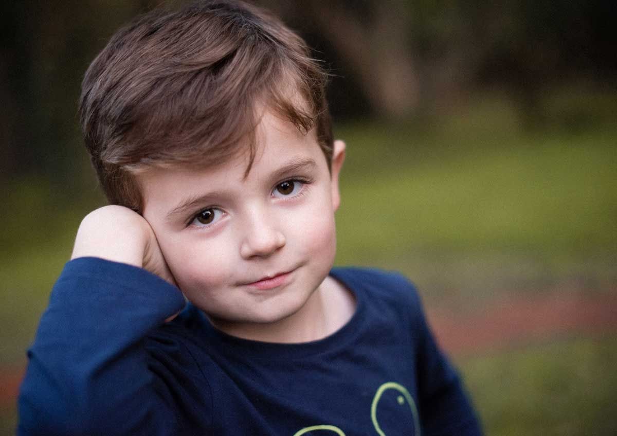 Young boy in a navy top resting his head on his hand against blurred bushland