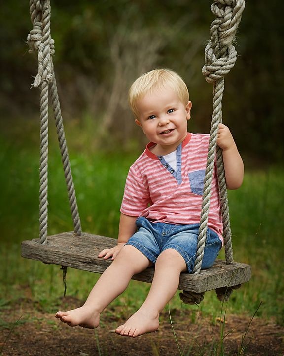 Barefoot toddler in a striped T-shirt sitting on a rope tree swing