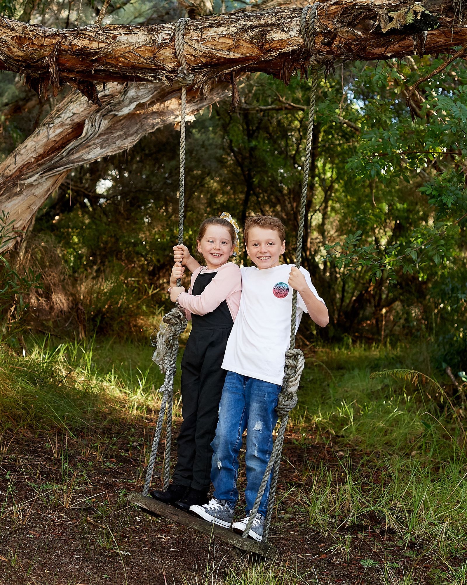 A brother and sister on the rope swing under the paperbark branch